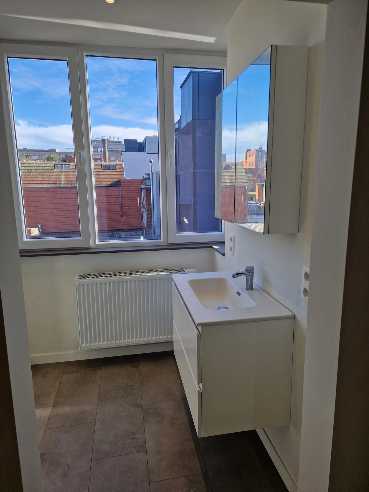 En-suite badkamer met modern lavabomeubel, spiegelkast en raam